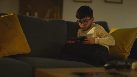 Young-Boy-Sitting-On-Sofa-At-Home-Playing-Game-Or-Streaming-Onto-Handheld-Gaming-Device-7
